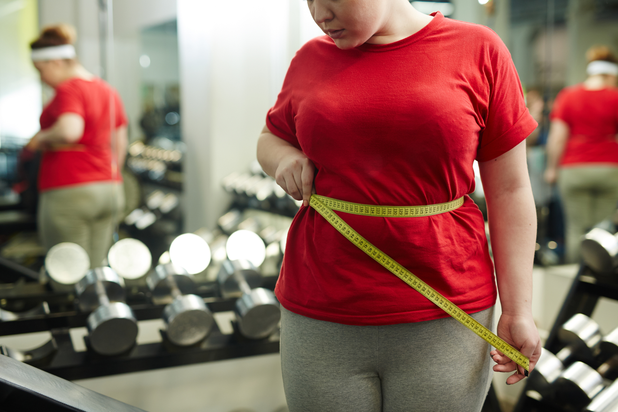Portrait of unrecognizable obese woman standing against mirror in gym and m...